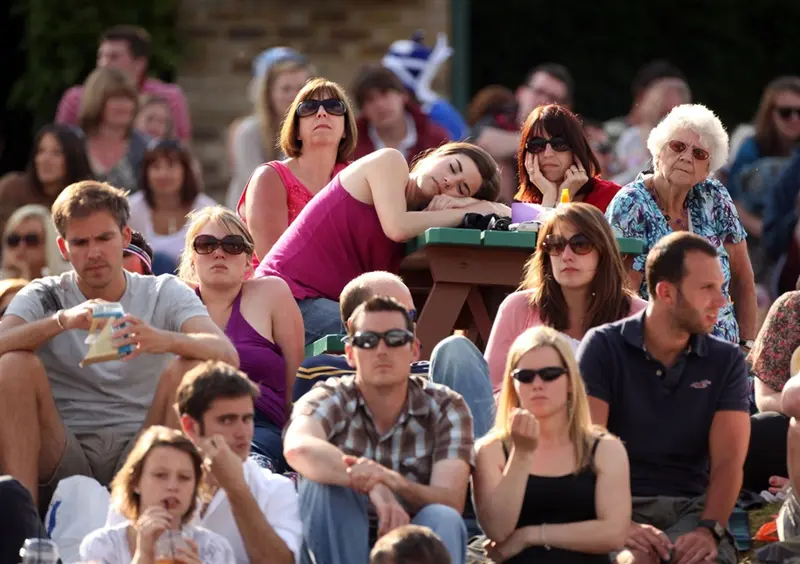Spectators sitting in the stands at Wimbledon, looking bored, one asleep on a table