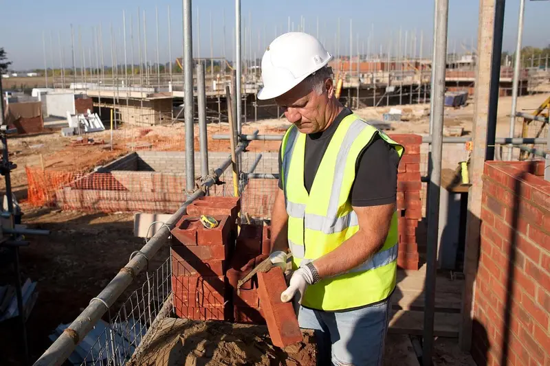 Bricklayer in a hard hat and hi-vis vest laying bricks on a building site