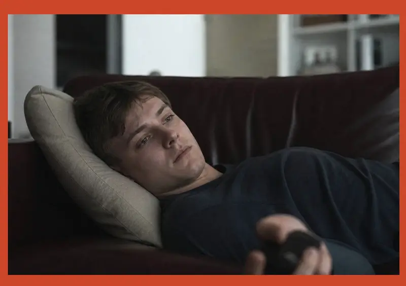Bored young man lying on a couch holding a remote, staring blankly