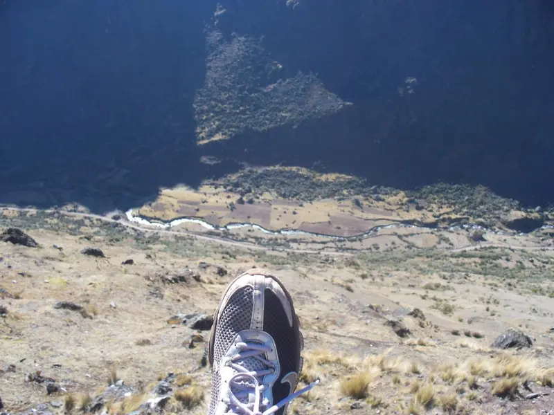 A sneaker poking over a steep mountain edge, high above a winding river in the valley below