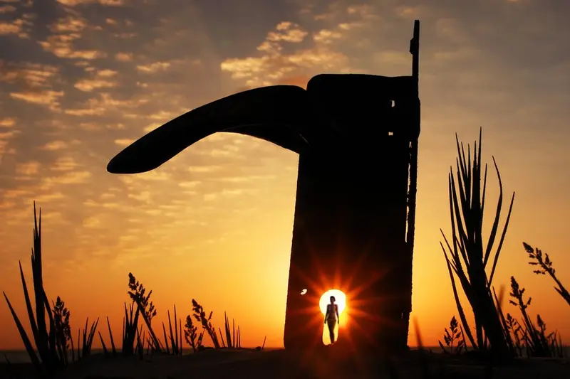 Sunset silhouette of a giant door handle, a tiny figure standing in a keyhole of light
