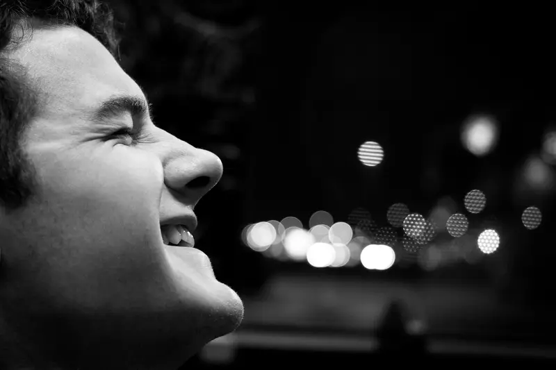 Black-and-white profile of a young man laughing, city lights blurred behind him