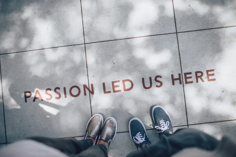 Two pairs of sneakers on a paved footpath beside the words PASSION LED US HERE