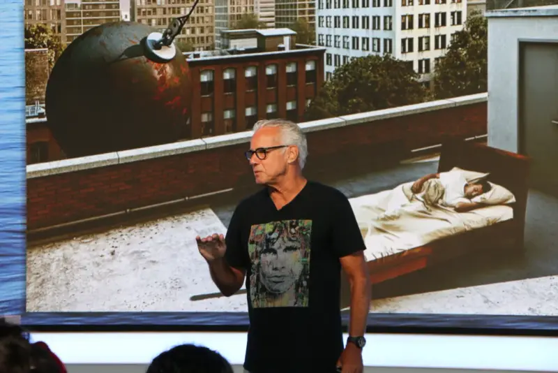 Richard on stage at the NGEN creativity session, in front of a surreal image of a bed on a rooftop and a wrecking ball