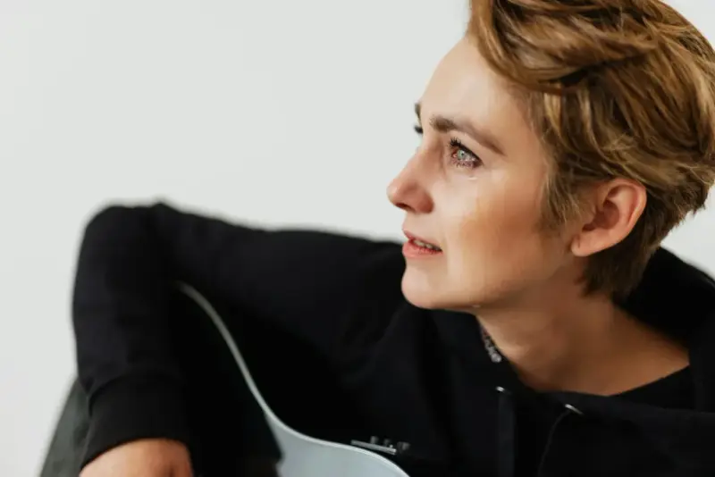 A tearful woman with short hair holding a guitar, gazing into the distance