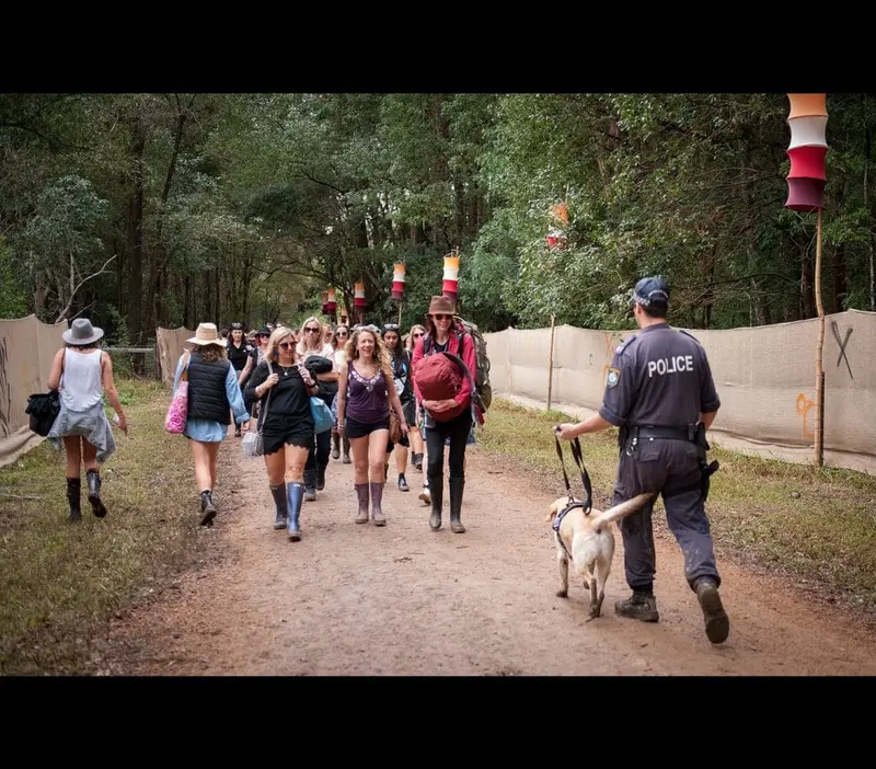 Police officer with a sniffer dog walking past festival-goers on a dirt path at Bluesfest