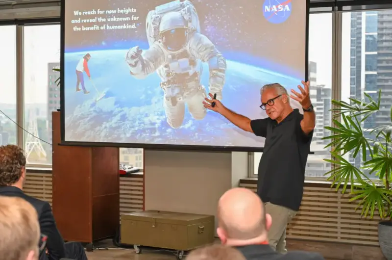 Richard speaking at a Big Pharma event in Melbourne, arms raised beside a slide of a NASA astronaut
